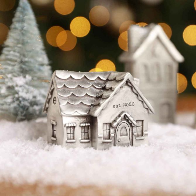 Our Cozy Cottage Christmas Village Add On, cast in pewter, displayed with the Winter Wonderland Village in fake snow