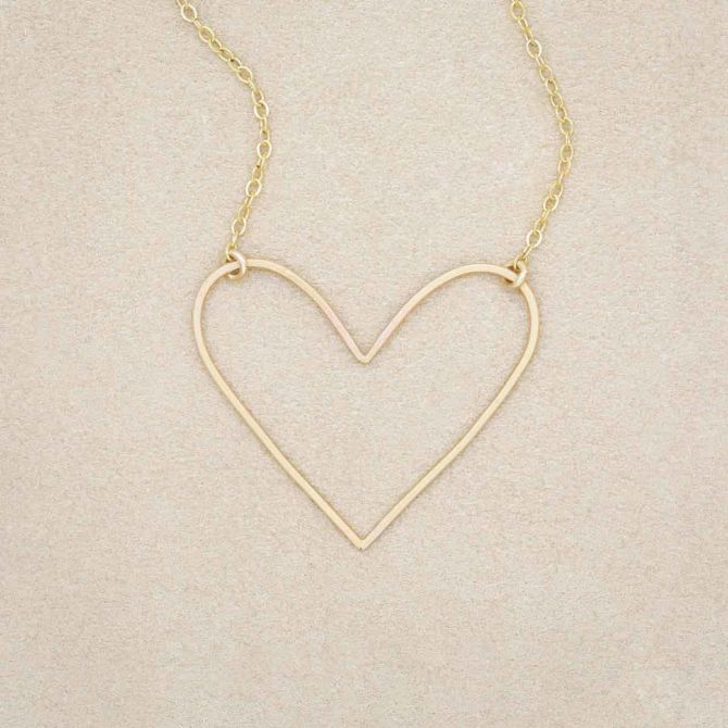 A gold filled Petite Peaceful Heart Necklace on beige background