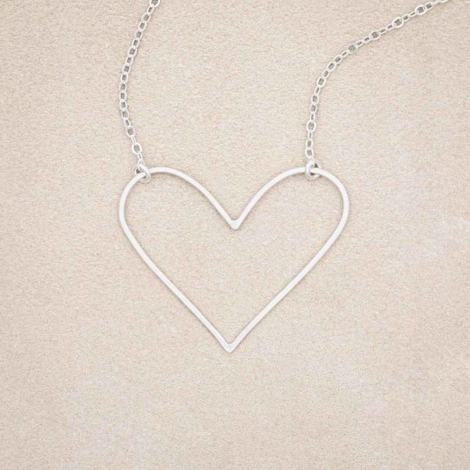 A sterling silver Petite Peaceful Heart Necklace, on beige background