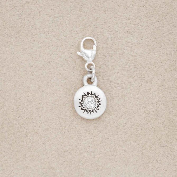 sterling silver Sunburst Bracelet Charm with a 3mm cubic zirconia, on a beige background