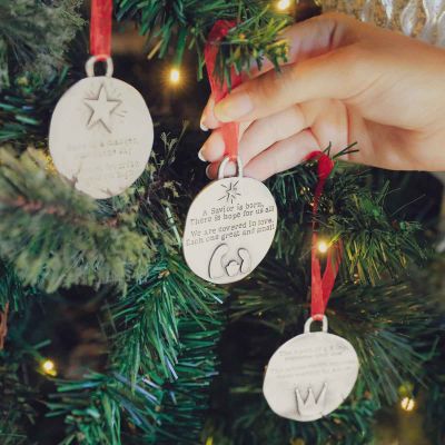 handcrafted babe in a manger pewter ornament set  hung on sheer red ribbon stamped with a Christmas story poem on Christmas tree