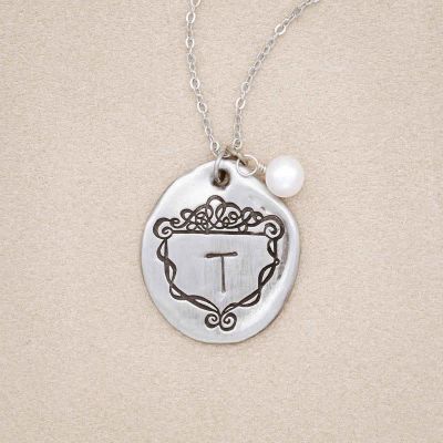 A Family Crest necklace handcrafted in pewter, customized with an initial and includes a freshwater pearl
