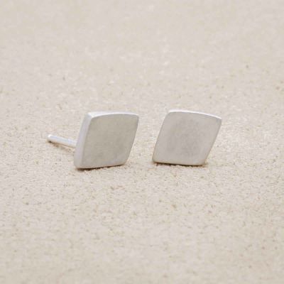 a pair of Fly A Kite Stud Earrings, handcrafted in sterling silver, laying on a beige background