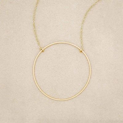 A gold filled It All Matters Circle Necklace, on beige background
