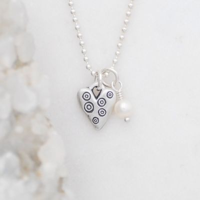 Light + Bright hearts necklace handcrafted in sterling silver with a matte brushed finish and the heart charm hung next to a vintage freshwater pearl