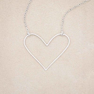 A sterling silver Petite Peaceful Heart Necklace, on beige background