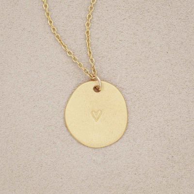 small and mighty heart disc necklace gold plated, on beige background